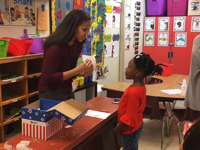 Hayden Hicks helps a first grader put her ballot in the box. 