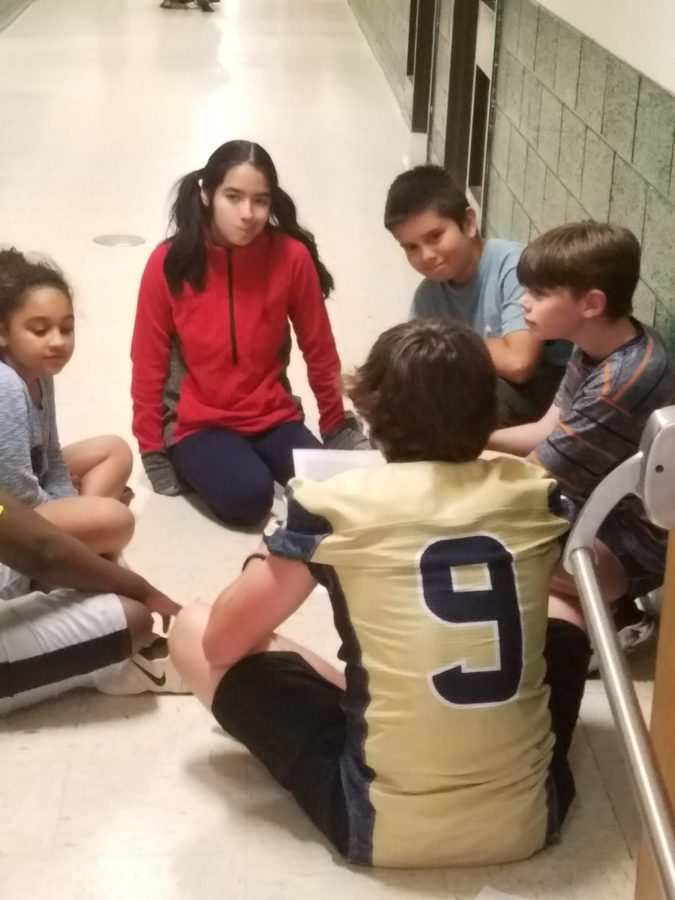 A group of students crowd around a Midlo football player, who eagerly answers their questions.