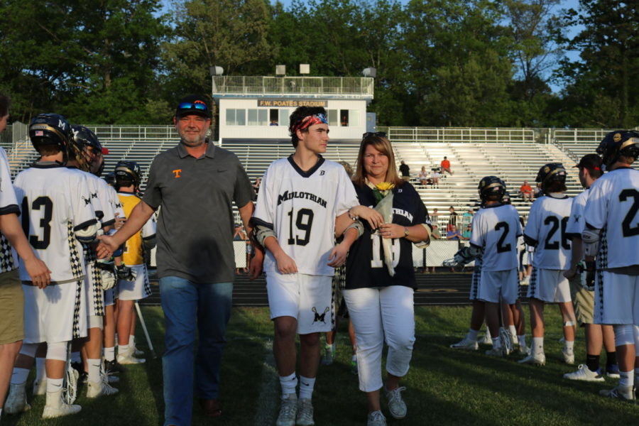 Tyler Schrimpsher, escorted by his mother and his father, takes the home field for one last time on his senior night.