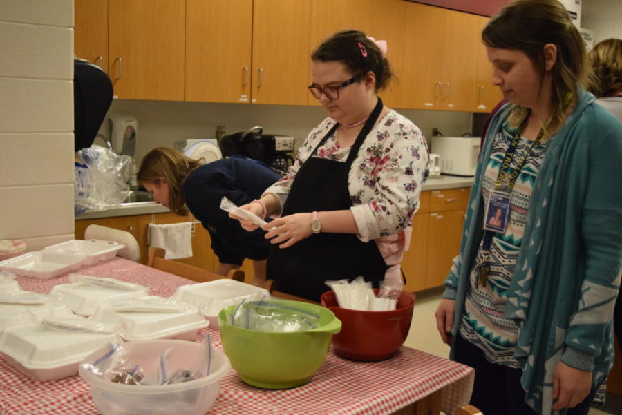 Autism teacher, Mrs. Randrianasolo watches as a student participant neatly stacks silverware onto the prepared potato trays in preparation for the potato bar. 