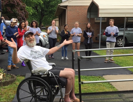 Midlo RAMPS client, Chad, successfully rolls down his newly built ramp and celebrates with  jazz hands and a group applause. 