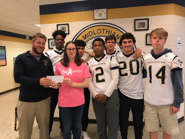 Coach Matt Hutchings, along with members of the Midlo Football team, hands their donation to Katy Sawyer from the Virginia Breast Cancer Foundation. 