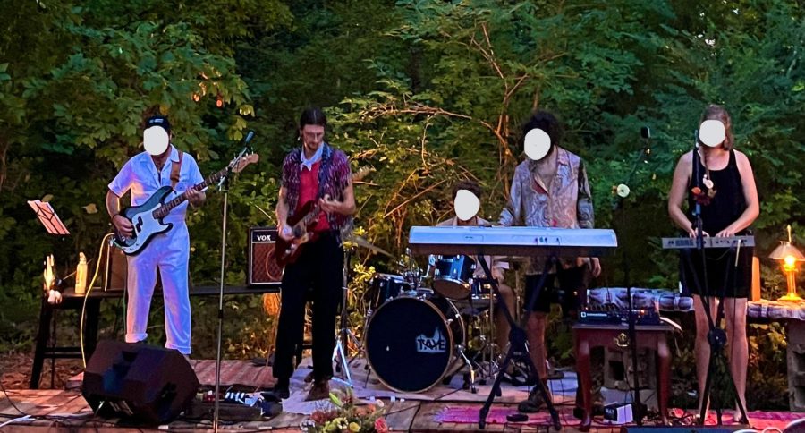 Micah Hadley playing with his guitar, along with the band he is in, at a venue.