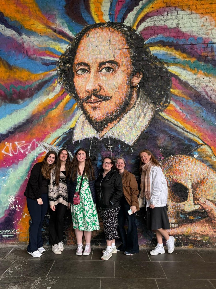 Students pose in front of a painting of Shakespeare.   